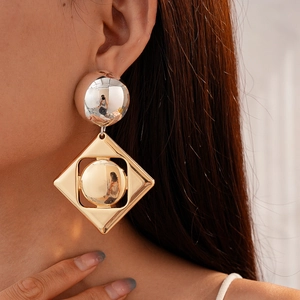 Close-up of geometric gold-toned earrings featuring metallic spheres and diamond frames