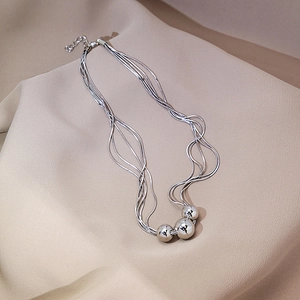 Detail of silver layered necklace with three polished spheres and snake chains on beige fabric