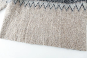 Close-up of beige knit sweater featuring dark grey wave patterns and fuzzy mohair texture