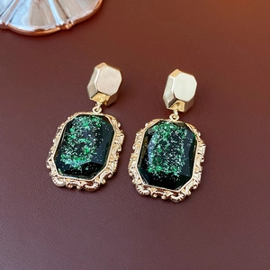 Detail of vintage gold earrings with green emerald resin and floral embossed frames