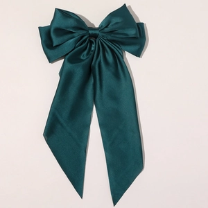 Macro detail of dark green satin bow hair clip with long elegant flowing ribbons