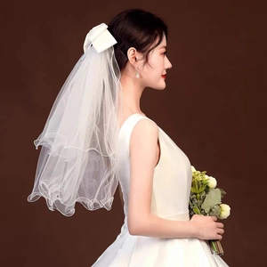 Detail of white double-layered bridal veil with satin bow and wavy edges on a model