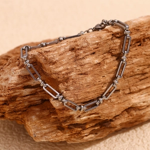 Detail of silver paperclip link chain anklet with round sphere clasp on a rock surface