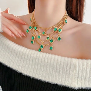 Close-up of a layered gold necklace featuring rectangular emerald green stones and rhinestones