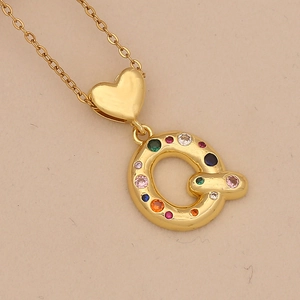 Close-up of golden heart pendant with colorful zircon letter Q on beige paper