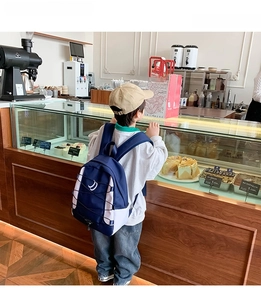 Donkerblauwe schoolrugzak met D-borduurwerk gedragen door een kind in een warme café-omgeving