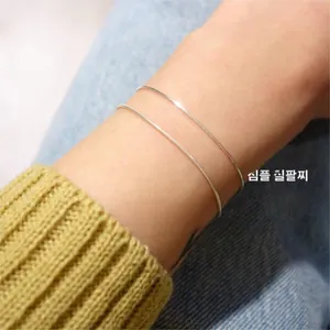 Close-up of dual minimalist silver snake bone chain bracelets worn on a female wrist