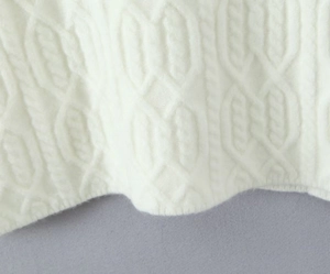 Close-up of white cable knit dress showing thick wool texture and intricate patterns