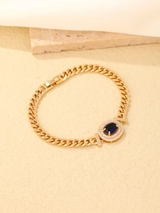 Macro detail of gold-plated bracelet with blue oval gemstone and cubic zirconia setting