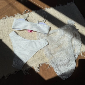 Detailed view of white three-piece bikini set with floral lace sarong and textured fabric