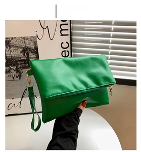 Detalle de cartera de mano tipo sobre verde en cuero PU con cremallera dorada y asa
