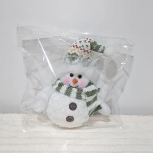 Close-up of a Christmas snowman plush with green knit hat and scarf in packaging
