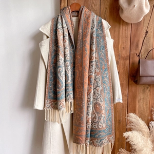 Close-up of orange paisley cashmere-style scarf with fringe on a white coat
