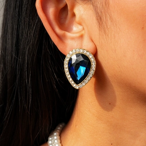 Gros plan d'une boucle d'oreille goutte avec pierre bleue et détail du collier de perles