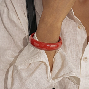 Detailed view of thick red resin round bangle worn with a white linen shirt