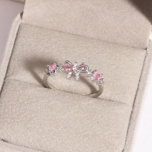Close-up of silver bow ring featuring pink heart-shaped stones and pavé accents