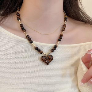 Detail of layered gold necklace featuring a leopard print heart pendant and tiger eye beads