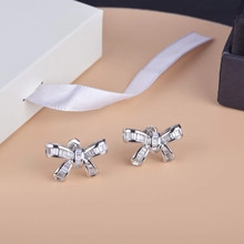 Detail of silver bow earrings with rectangular zircon stones on a beige gift background