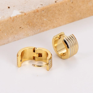 Golden ribbed hoop earrings with silver stripes displayed on a textured stone base