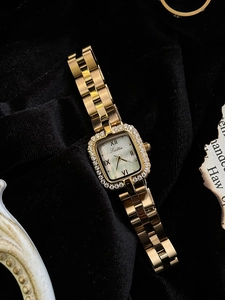 Détail d'une montre carrée dorée avec lunette en strass et cadran en nacre sur velours noir
