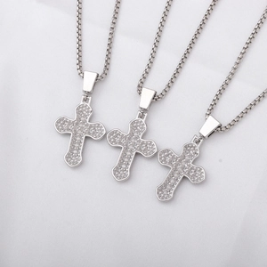 Macro detail of three silver cross necklaces with shimmering clear stones on white fabric