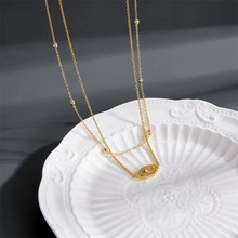 Detailed close-up of golden evil eye necklace with crystals on white ceramic plate