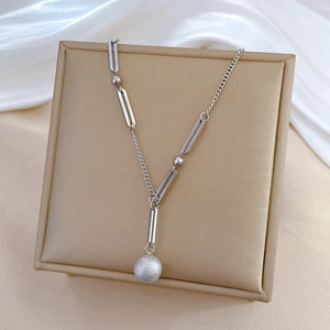 Macro detail of Y-shaped silver necklace with frosted ball pendant on a gold display box