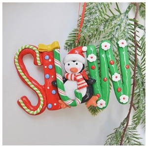 Close-up of a festive penguin polymer clay ornament with candy cane and snowy pine branch