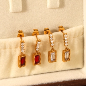 Detail of gold-plated rectangle gemstone drop earrings with pearls on white velvet