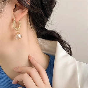 Close-up of golden woven C-shaped hoop earrings with elegant pearl drop on a model