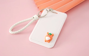 Detail of white cartoon card holder with woven wrist strap and carrot charm on pink background