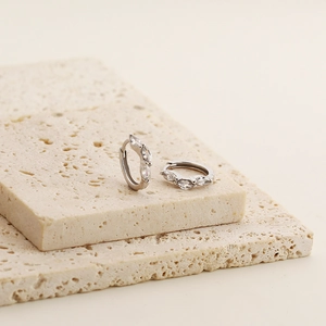 Close-up of s925 silver huggie earrings with marquise-cut zircons on beige travertine