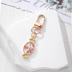 Detail of candy-shaped keychain with pink dried flowers on a white textured stone base