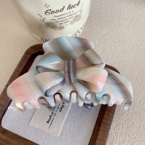 Détail d'une pince à cheveux nœud en acétate rose et bleu sur un plateau en bois