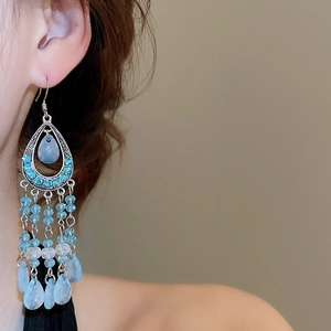 Detailed view of bohemian teardrop earrings with blue beads and silver tassels on model