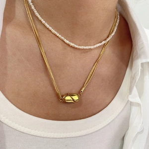 Close-up of layered gold snake chain with heart pendant and white pearl necklace