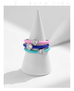 Detailed view of three S925 silver heart rings in pink, blue, and cyan on white stands
