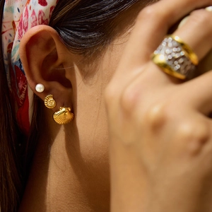 Close-up of elegant gold shell earrings and white pearl studs on woman's ear