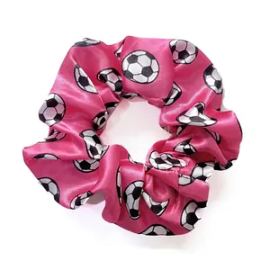 Detail of a bright pink satin scrunchie with classic soccer ball patterns and smooth texture