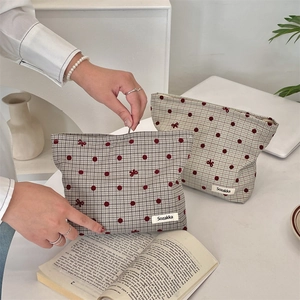 Dettaglio di pochette per cosmetici a quadretti kaki con pois rossi e ricami a fiocco