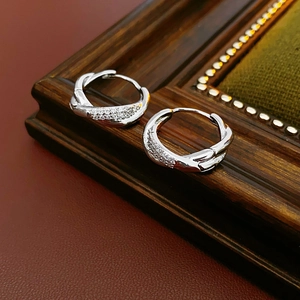 Detail of silver twisted hoop earrings with tiny clear zircons on dark wood frame