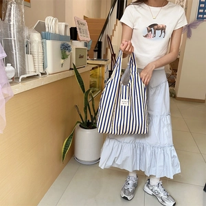 Detail of blue and yellow striped canvas tote bag worn in a casual lifestyle setting