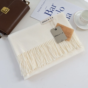Close-up of soft beige cashmere scarf with long tassels and woven label on aesthetic layout