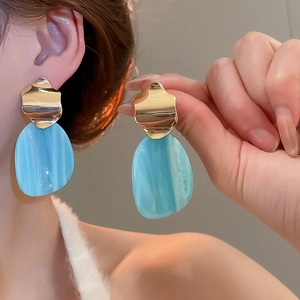 Macro shot of gold irregular oval earrings with marble-textured light blue resin pendants