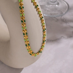 Detail of 18K gold-plated necklace with green enamel leaves on a white ceramic stand
