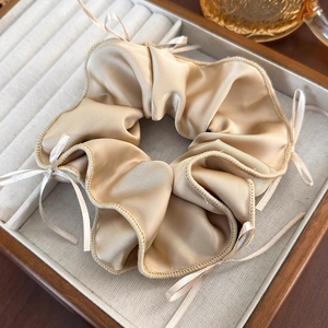 Close-up of champagne silk scrunchie with delicate bow detail in a wooden box