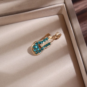 Gros plan d'une broche violon dorée avec strass bleus sur écrin en soie beige