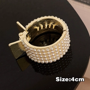 Detail of 4cm gold metal hair claw with white pearls on a black reflective surface