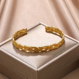 Detailed macro view of a gold-plated woven texture open bangle on a satin gift box