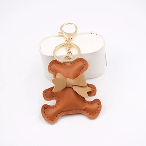 Detail of brown PU leather bear keychain with beige bow and gold lobster clasp hardware